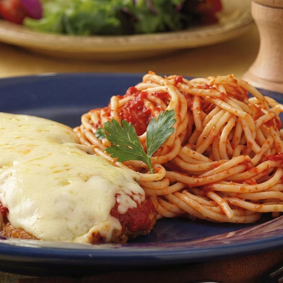Chicken Parmesan topped with melted cheese and marinara, served with spaghetti in tomato sauce on a blue plate.